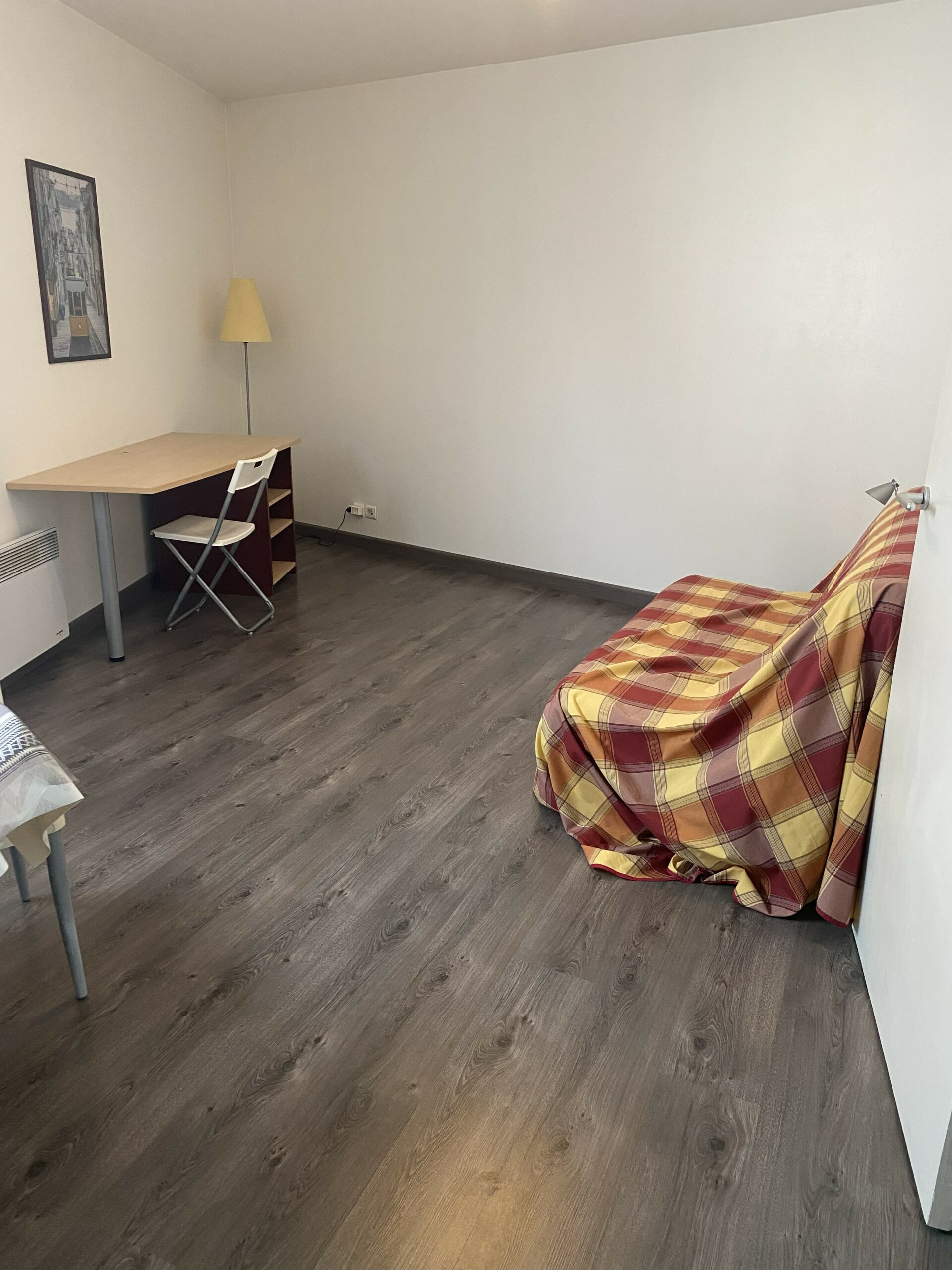 Séjour avec parquet sombre, canapé convertible à motif écossais rouge et coin repas.