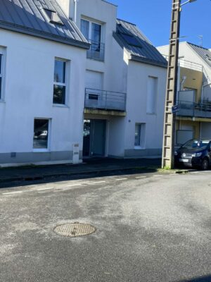 Façade d'une résidence moderne sous un ciel bleu avec places de stationnement à proximité.