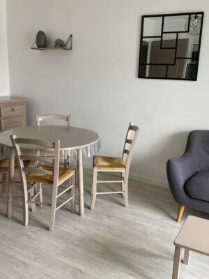 Pièce de vie avec table ronde en bois, chaises assorties et canapé gris confortable sur parquet clair.