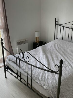 Lit double avec cadre en métal noir placé près d'une fenêtre lumineuse dans une chambre sobre.