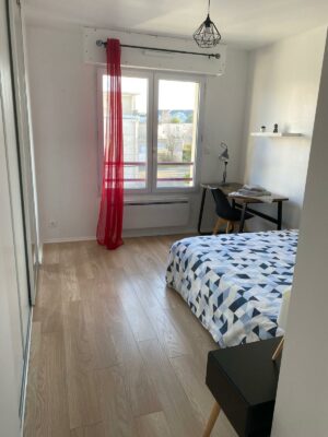 Chambre lumineuse avec lit double, parure de lit géométrique et bureau intégré près de la fenêtre.
