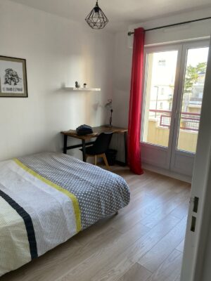 Chambre lumineuse avec lit double, parure de lit géométrique et bureau intégré près de la fenêtre.