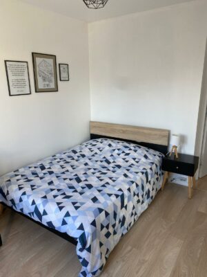 Chambre lumineuse avec lit double, parure de lit géométrique et bureau intégré près de la fenêtre.