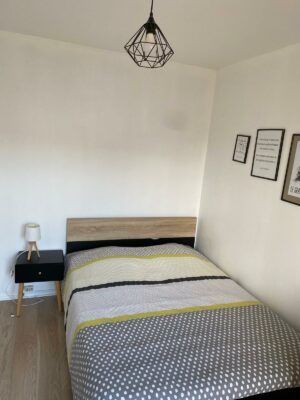 Chambre lumineuse avec lit double, parure de lit géométrique et bureau intégré près de la fenêtre.