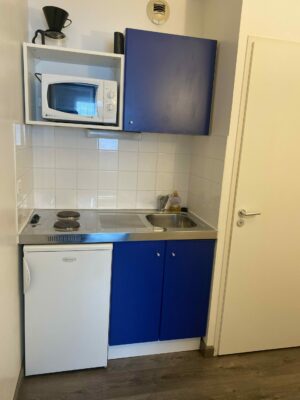 Petite cuisine fonctionnelle avec meubles bleus, micro-ondes et plaques électriques.