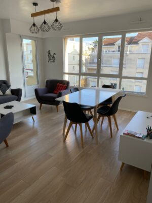 Salon moderne avec parquet clair, canapé gris anthracite et table à manger blanche épurée.