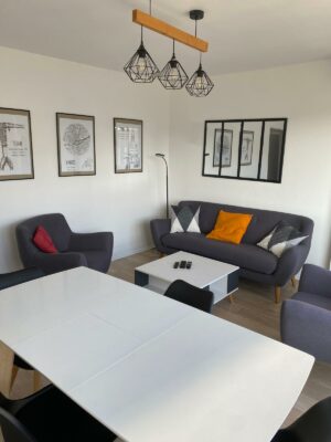 Salon moderne avec parquet clair, canapé gris anthracite et table à manger blanche épurée.