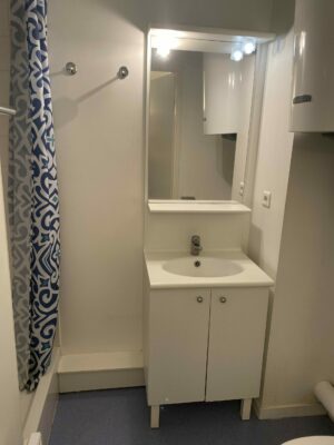 Salle d'eau compacte avec meuble vasque blanc, miroir et rideau de douche bleu.