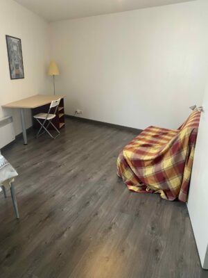 Séjour avec parquet sombre, canapé convertible à motif écossais rouge et coin repas.
